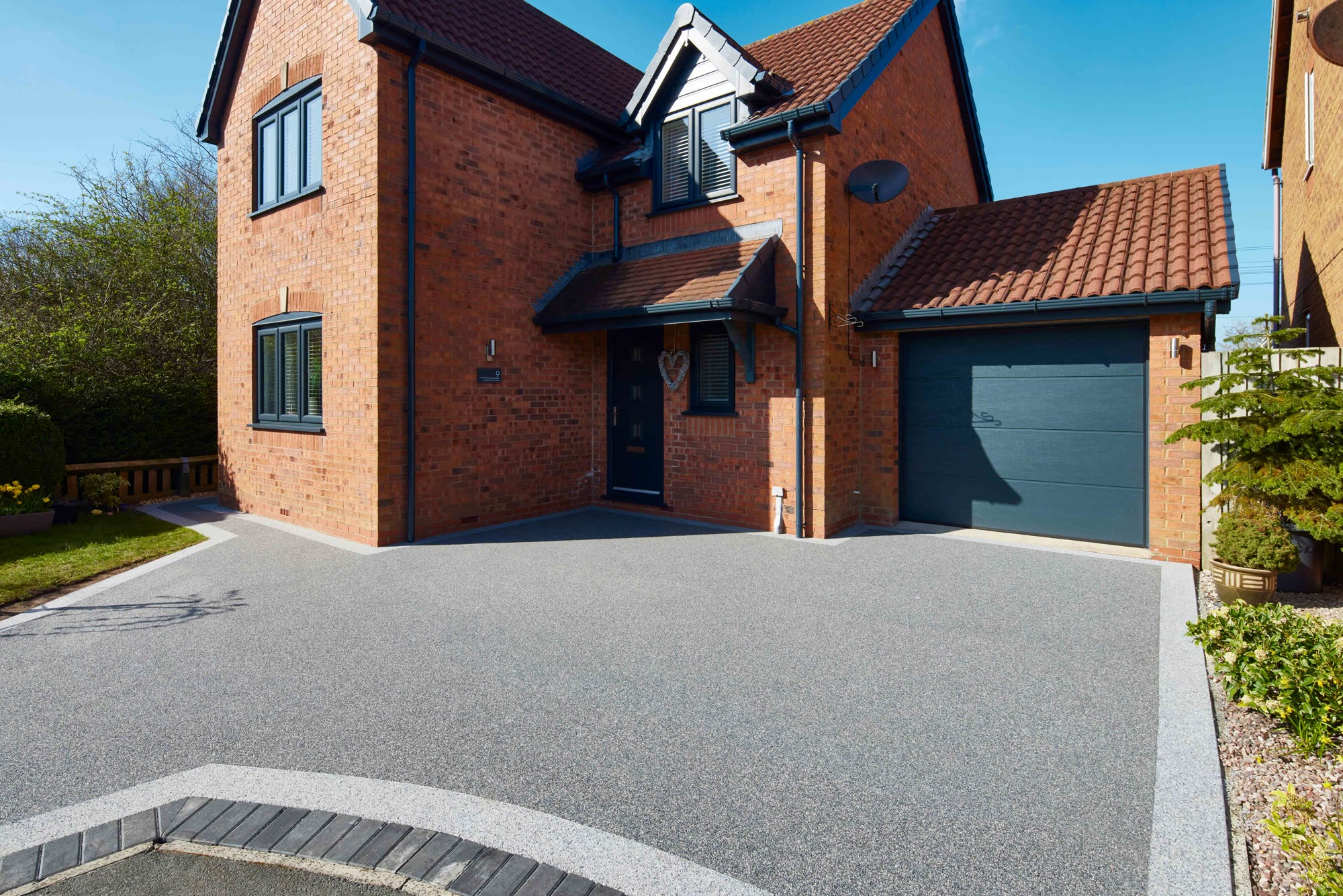 Gray Vuba Stone driveway with a light border in front of a brick house